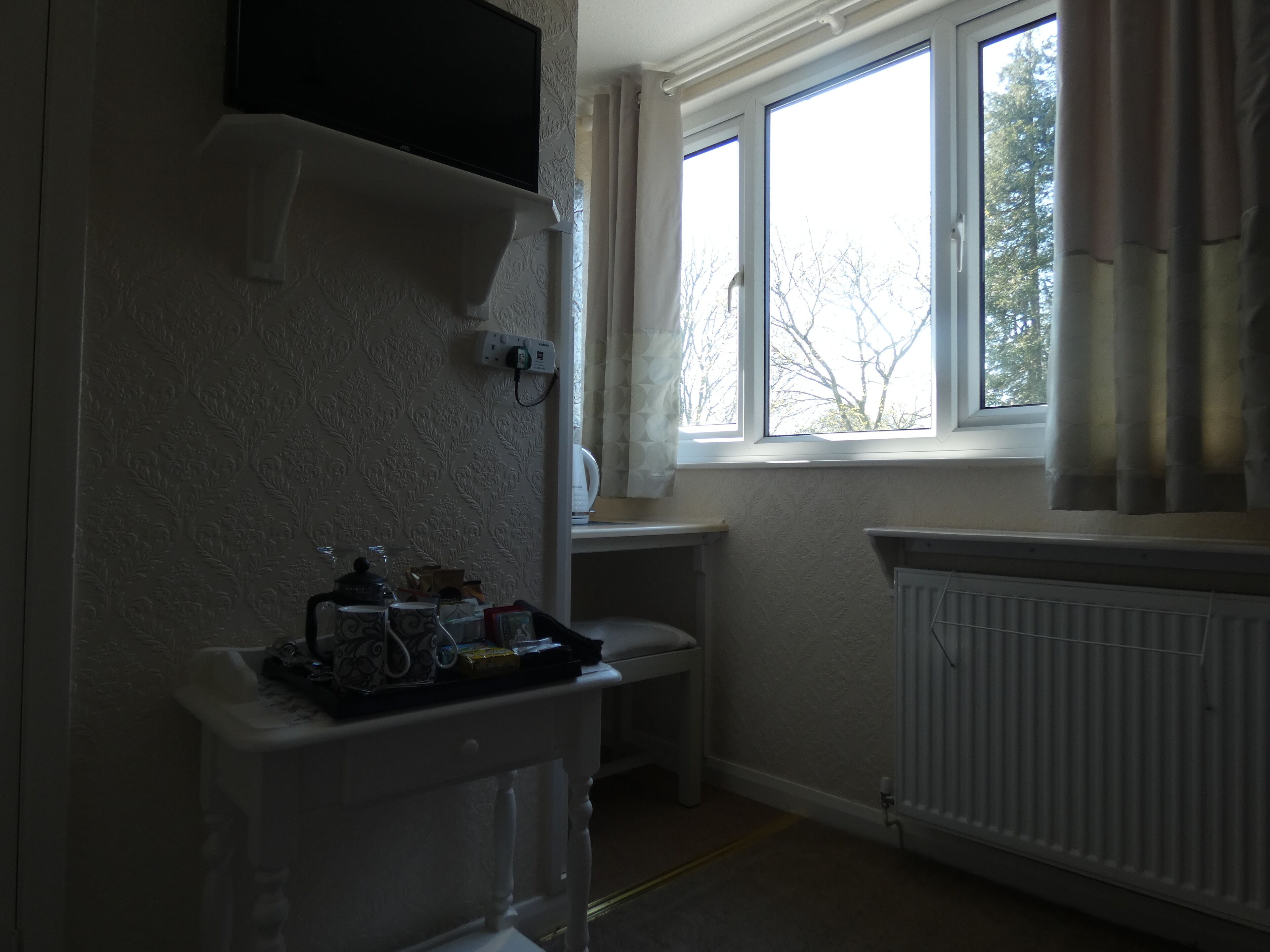 A small, dimly lit room with a radiator, a window with curtains, and a television mounted on the wall.