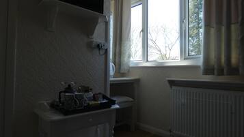 A small, dimly lit room with a radiator, a window with curtains, and a television mounted on the wall.