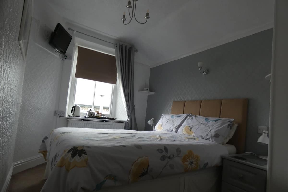 Una camera da letto con un letto, un comodino, una lampada e una TV fissata alla parete.