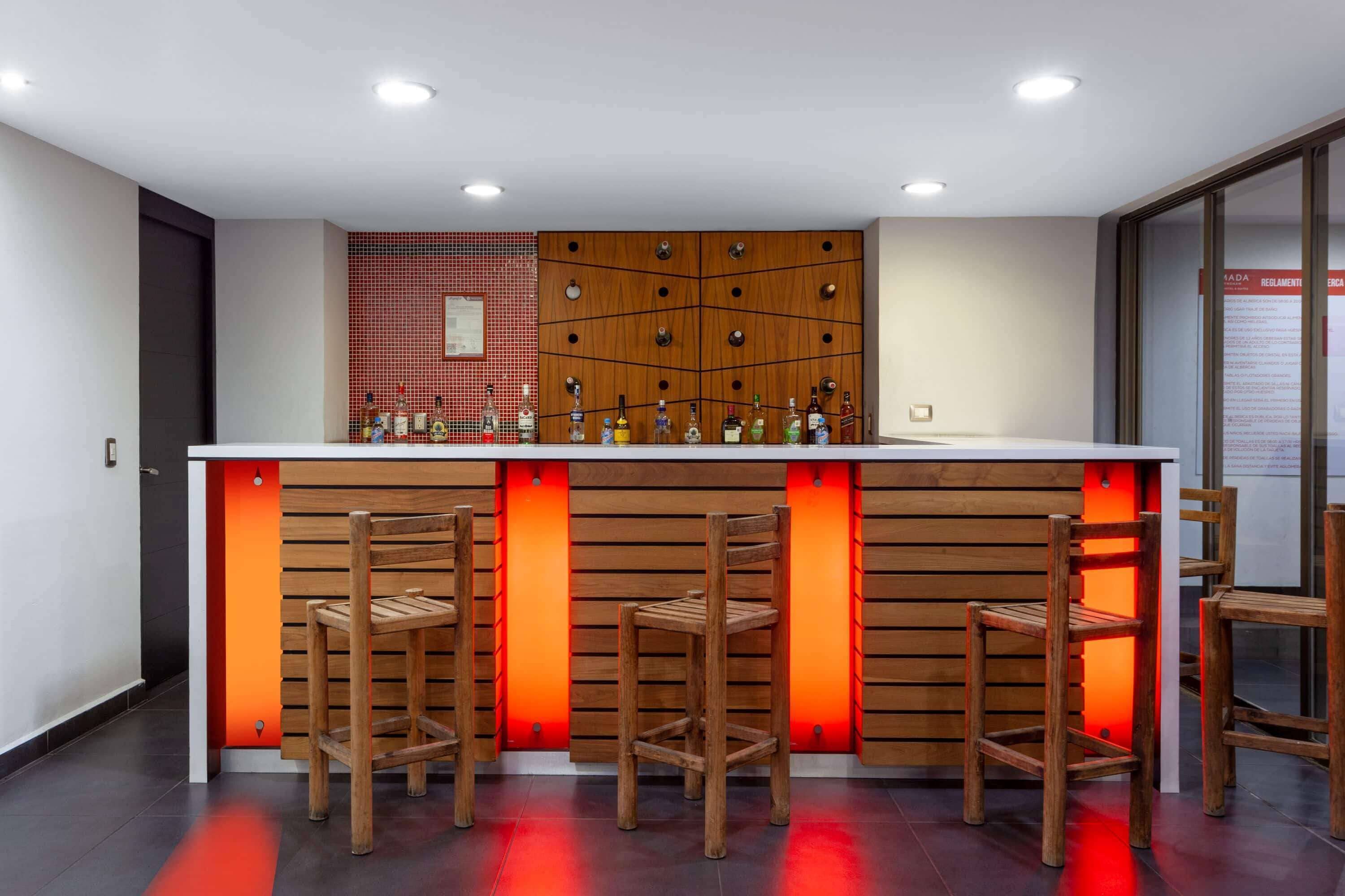 A modern bar area with wooden stools, a white countertop, and a red-tiled wall.
