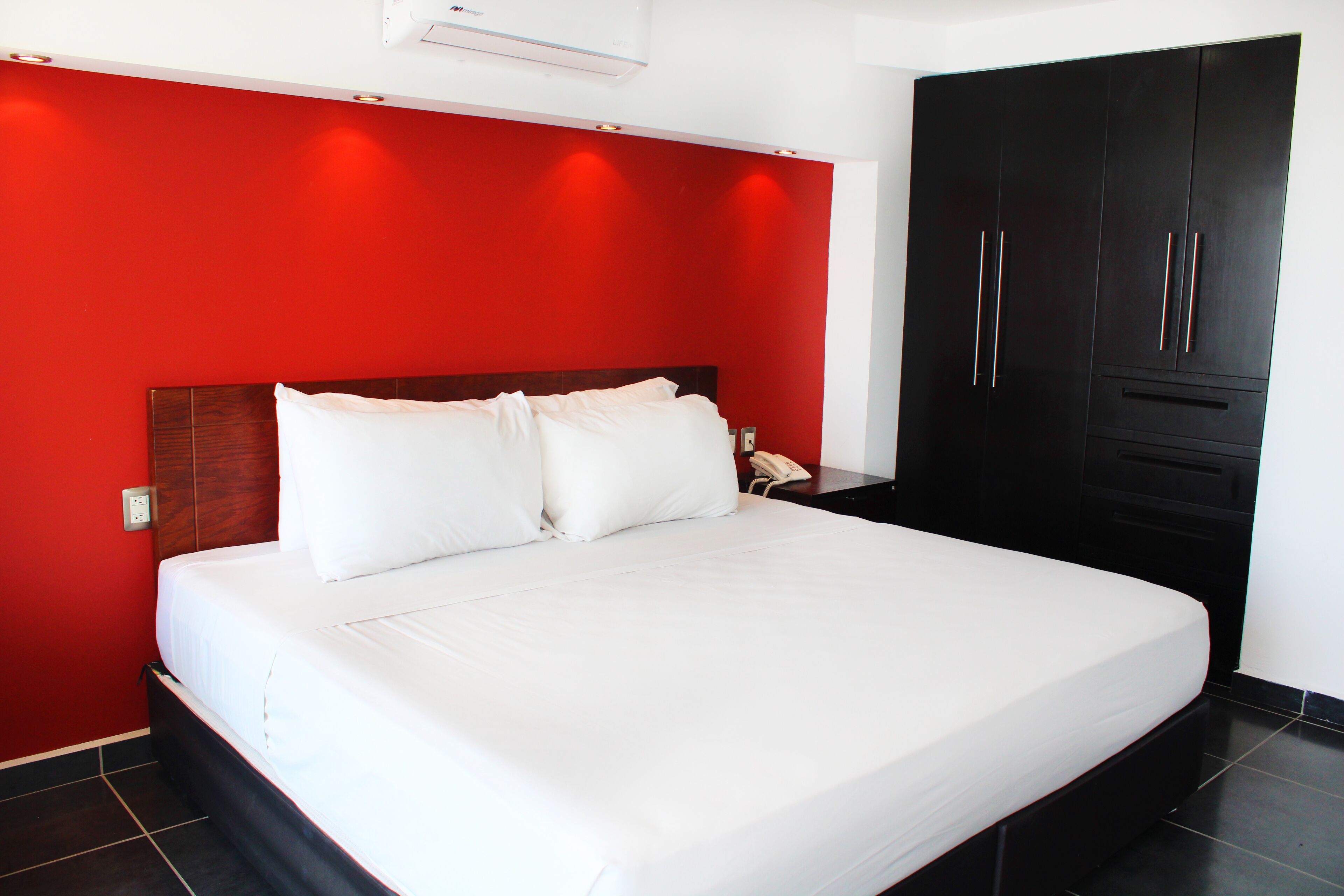 A hotel room with a large bed, red walls, and a black wardrobe.