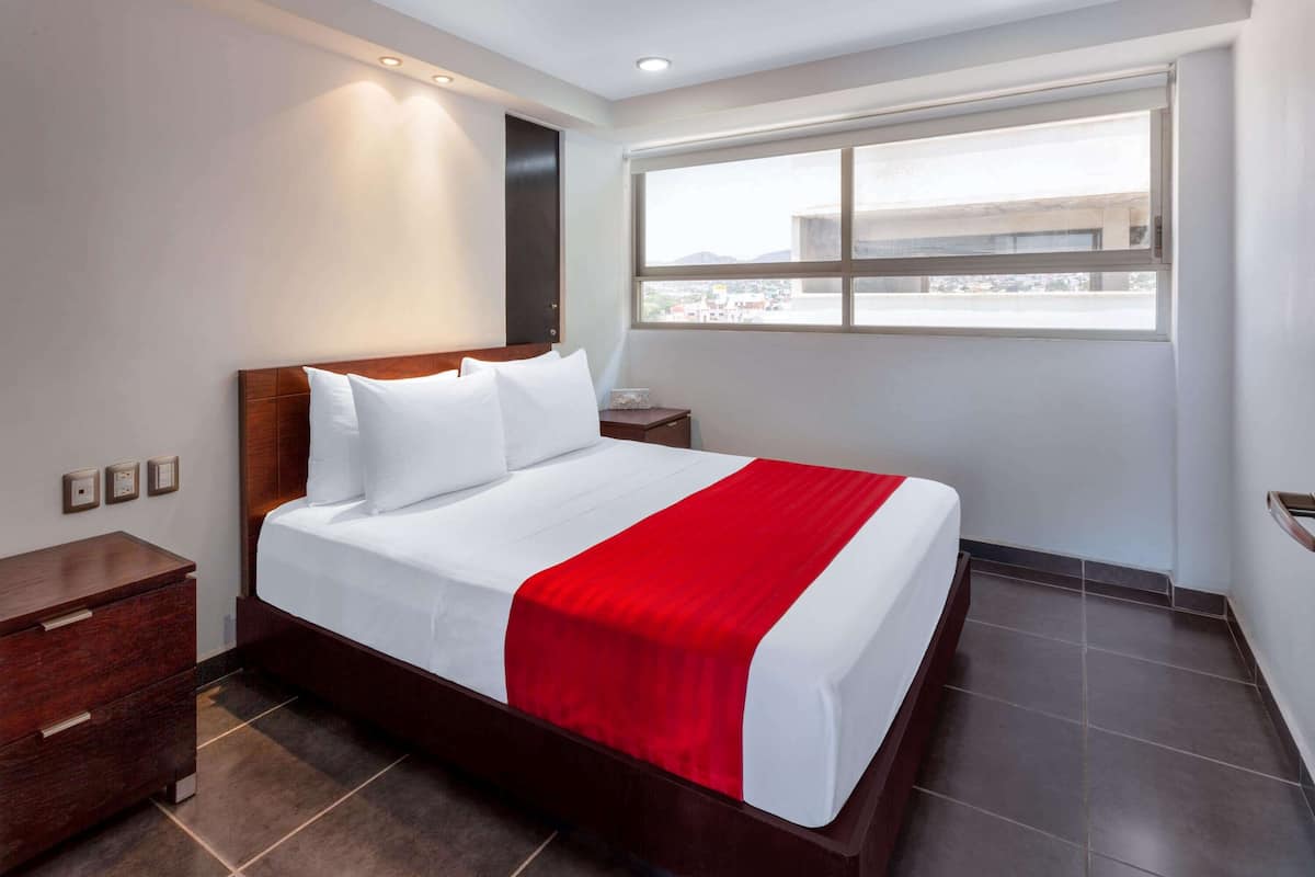 Een hotelkamer met een groot bed, een nachtkastje, een houten dressoir en een raam met uitzicht op de stad.