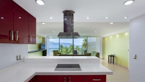 A modern kitchen with red cabinets, a white countertop, and a view of a green outdoor area.