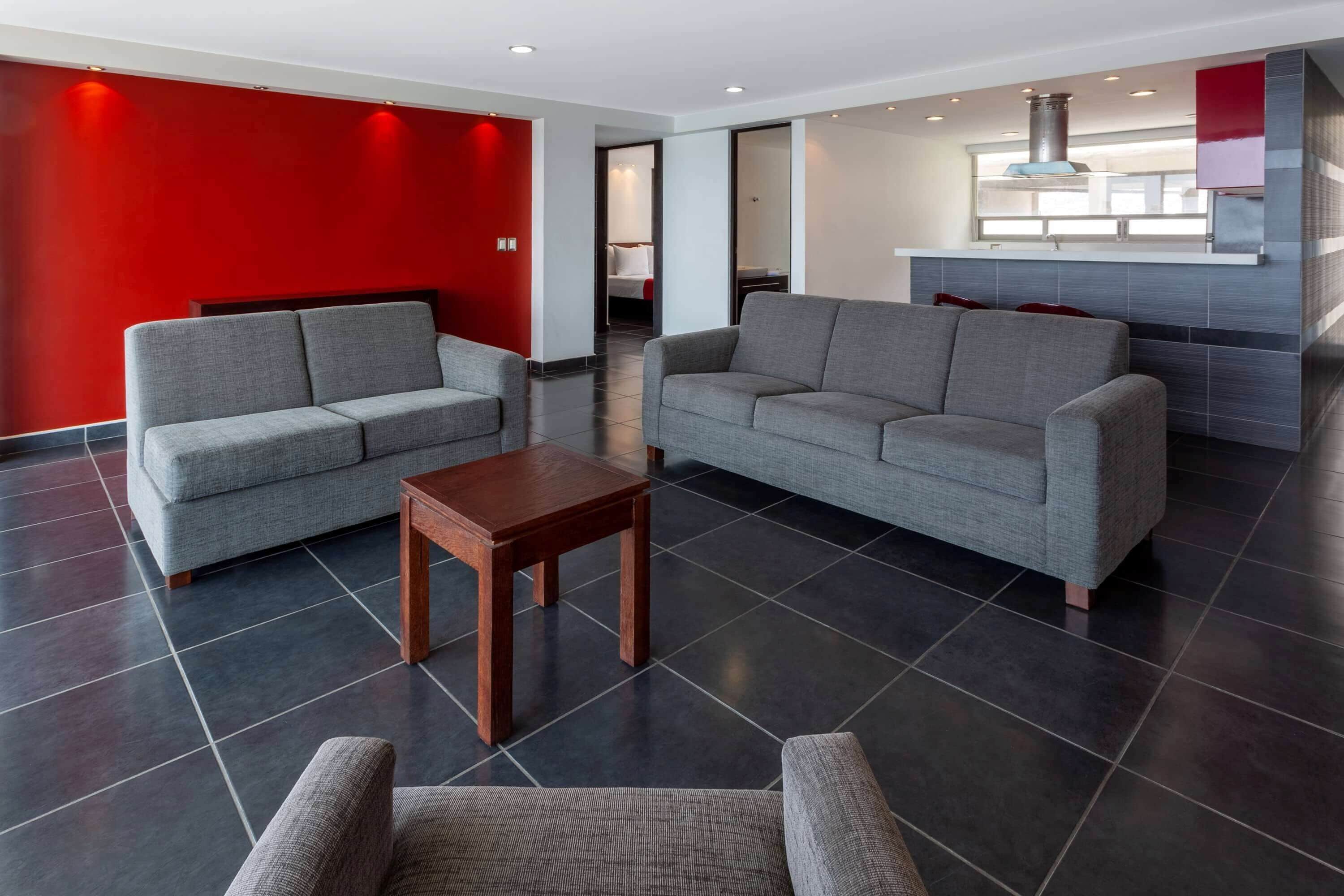 Un moderno vestíbulo de hotel con sofás grises, una mesa de madera y una pared roja de acento.