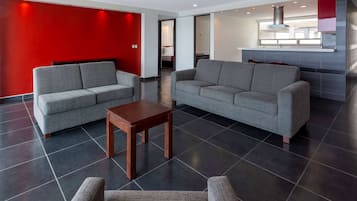 Um hall de hotel moderno com sofás cinza, uma mesa de madeira e uma parede de destaque vermelha.