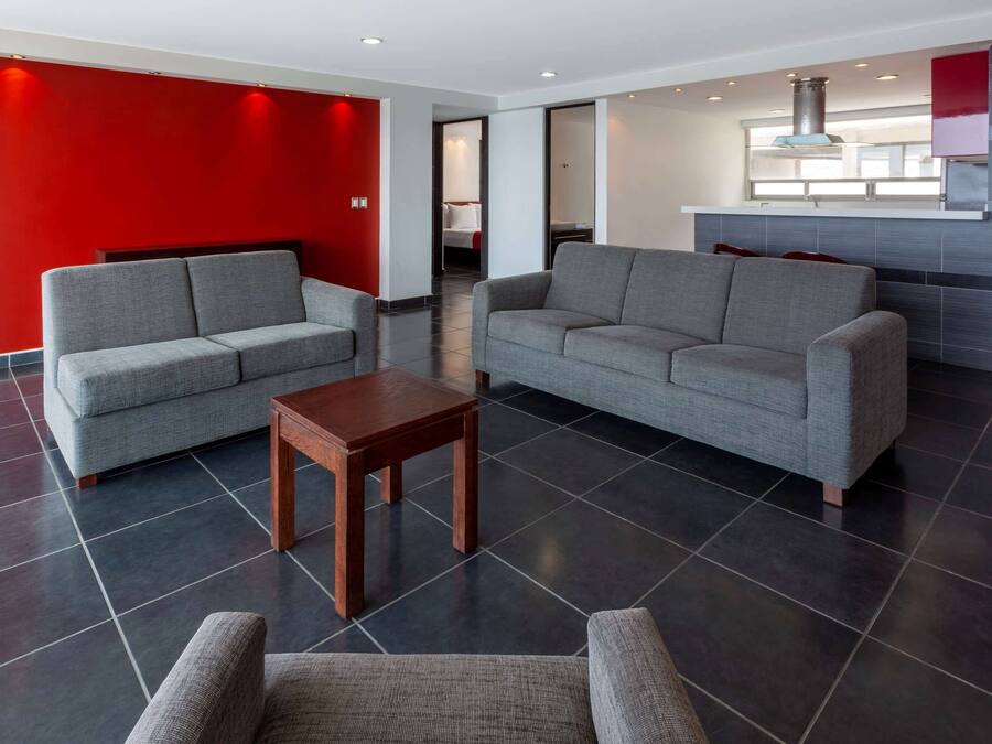 Um hall de hotel moderno com sofás cinza, uma mesa de madeira e uma parede de destaque vermelha.
