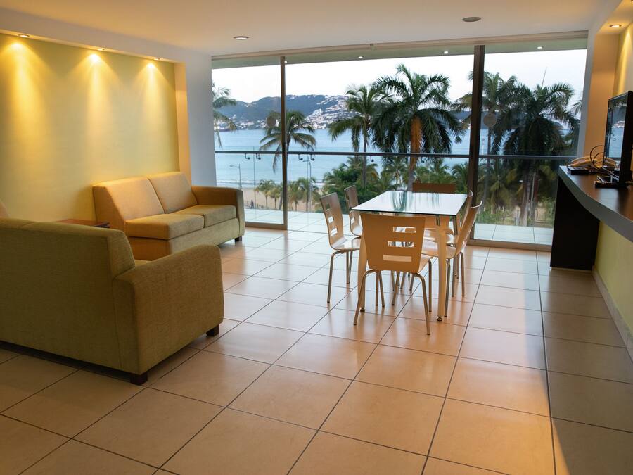 A spacious living area with a balcony overlooking a beach and palm trees.