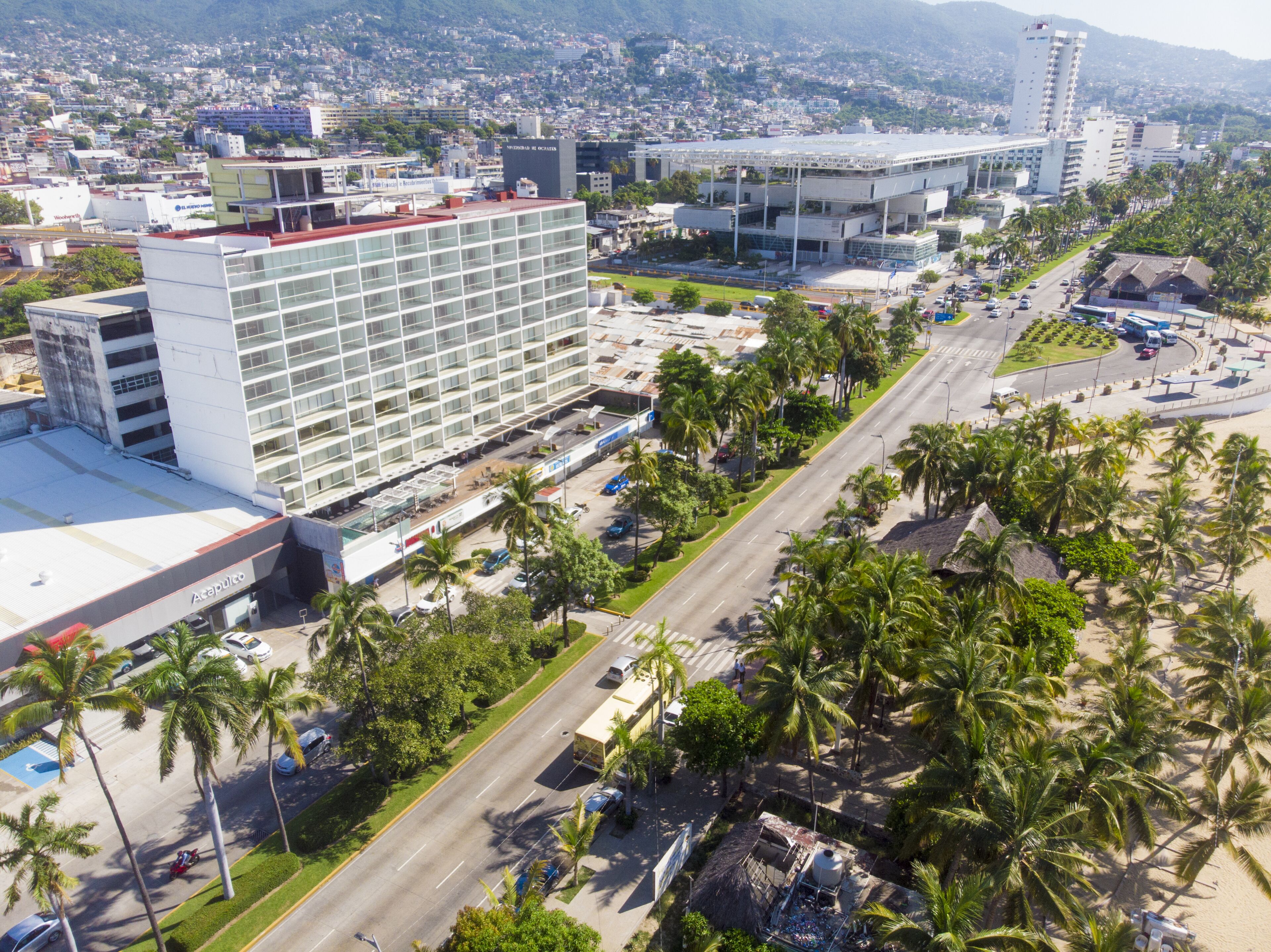 Un hotel moderno con una amplia fachada de vidrio, una terraza en la azotea y un estacionamiento.