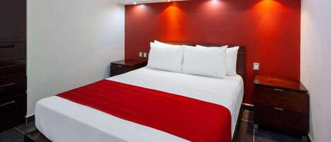 A modern hotel room with a large bed, red accent walls, and a built-in air conditioning unit.