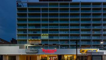 A multi-story hotel with a prominent 'Ramada' sign, featuring a modern architectural design with balconies and a flat roof.