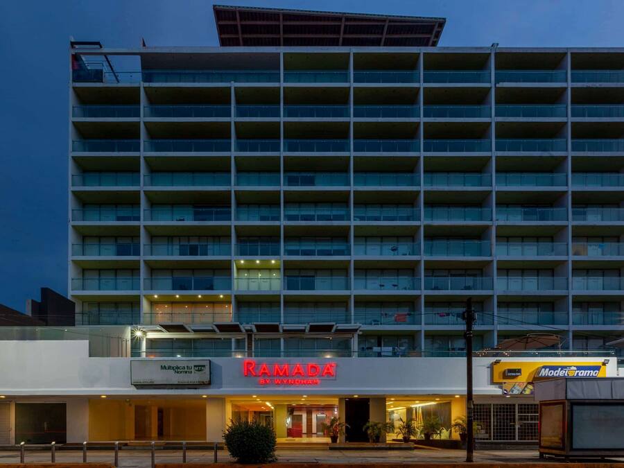 A multi-story hotel with a prominent 'Ramada' sign, featuring a modern architectural design with balconies and a flat roof.