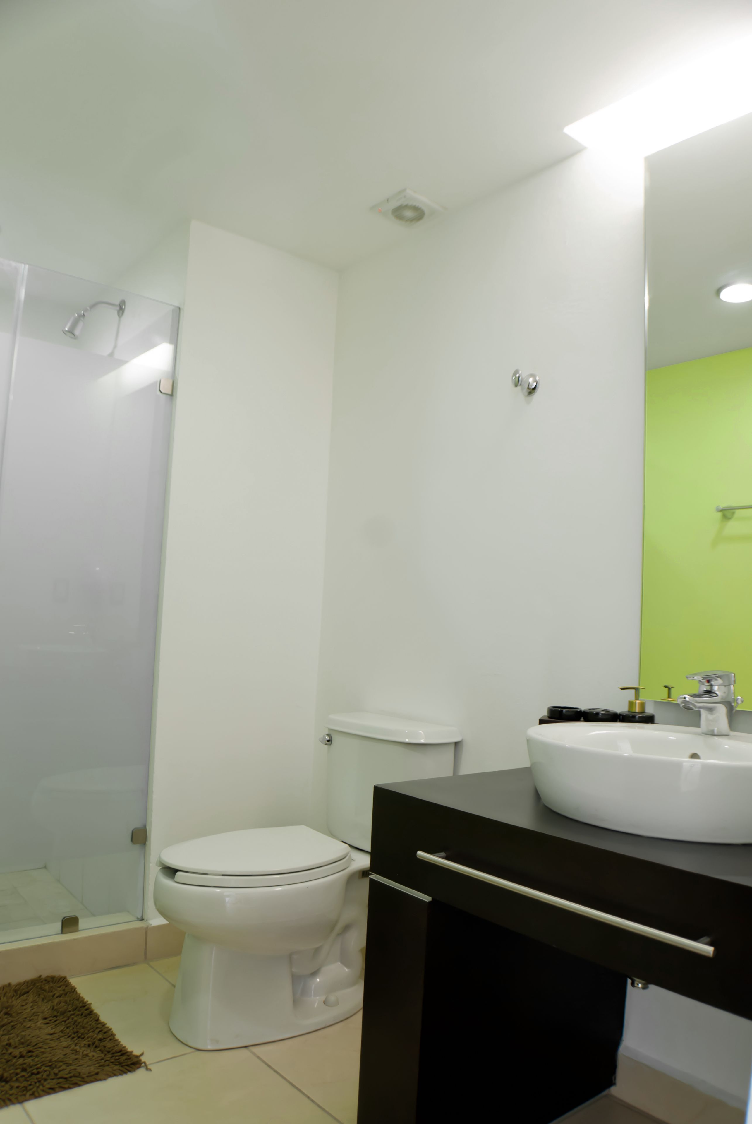 A bathroom with a white toilet, a black vanity, a white sink, and a green accent wall.