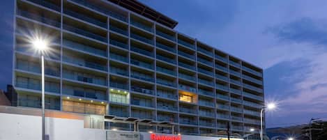 Un hotel de varios pisos con un diseño moderno, que presenta un llamativo letrero de 'Ramada' y el logotipo de un banco 'BBVA'.