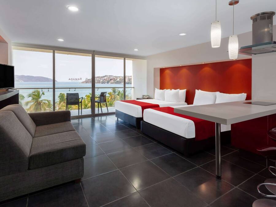 A modern hotel room with a balcony, a sofa, a bed with white bedding, and a dining area.