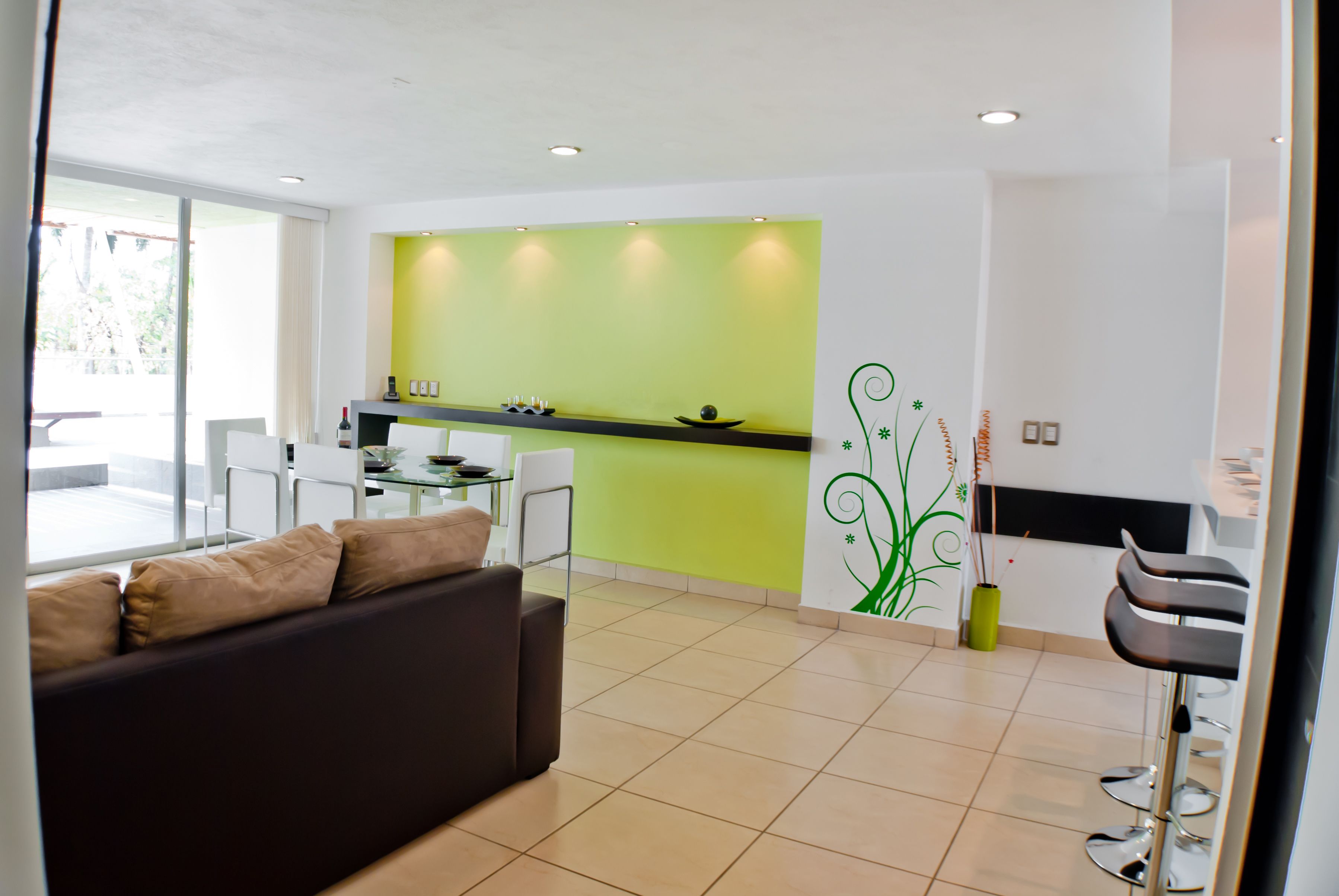 Una sala de estar moderna con un sofá, un comedor y una cocina con una pared verde de acento.