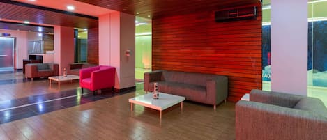 Un vestíbulo moderno con piso de madera, pared roja y zonas de estar que incluyen un sofá rojo y un sofá gris.