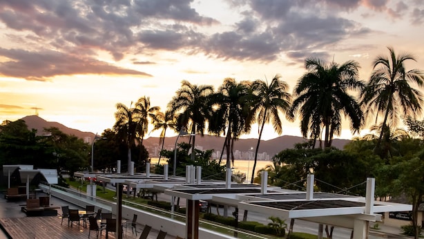 A pool area with lounge chairs and a view of palm trees and mountains in the background.