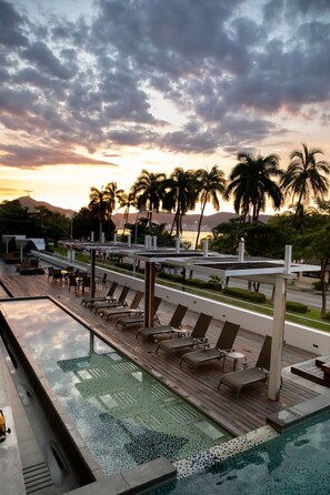 A pool area with lounge chairs and a view of palm trees and mountains in the background. - Ramada by Wyndham Acapulco Hotel & Suites (Acapulco)