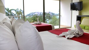 A hotel room with two beds, a red and white color scheme, a flat-screen TV, and a view of palm trees and mountains.