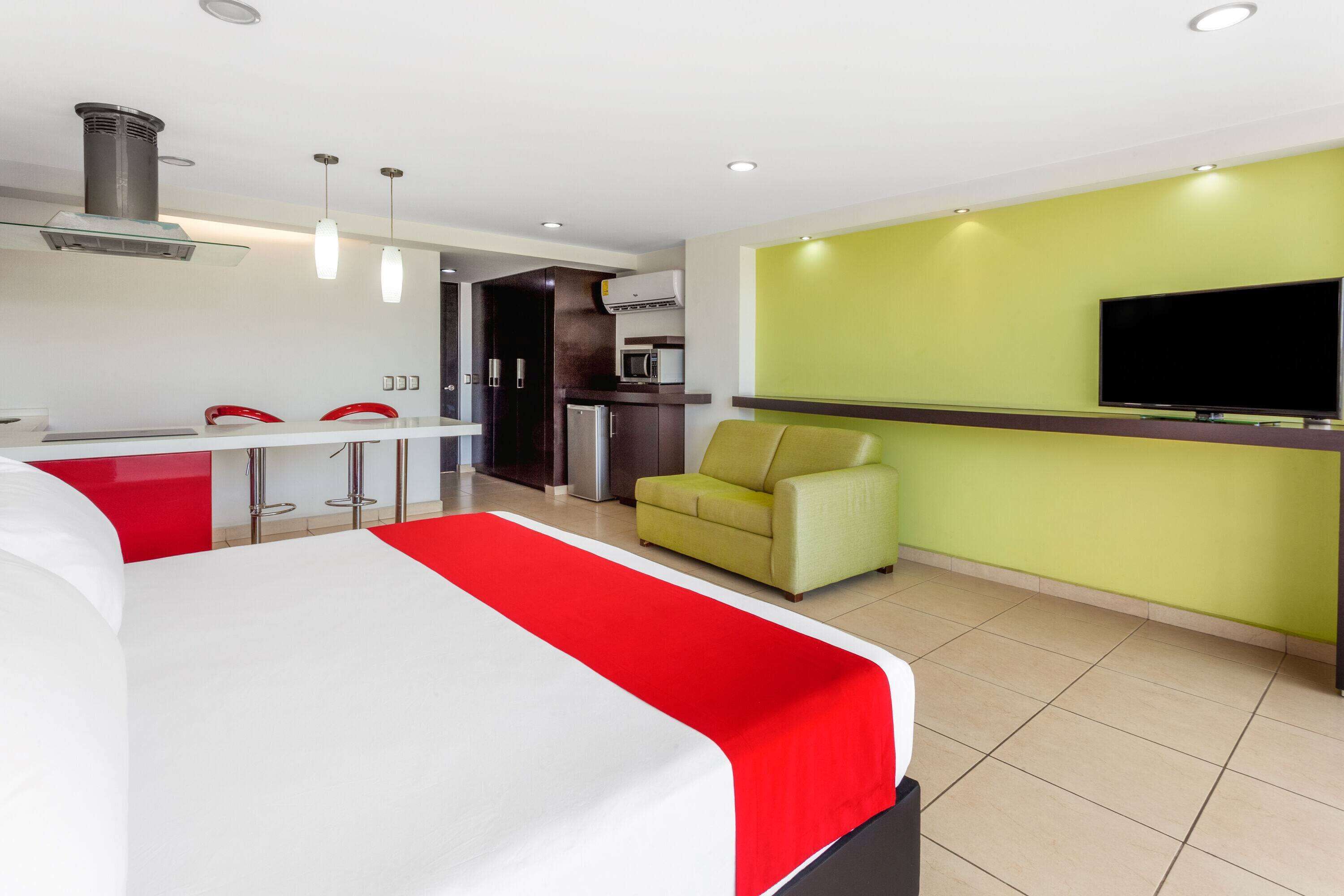 A hotel room with a bed, a TV, a kitchenette, and a sofa.