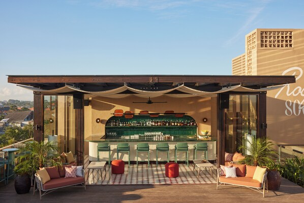 Eine Außenbar mit modernem Design, inklusive Bar, mehreren Hockern und einer Sitzecke mit Sofa und Sesseln.