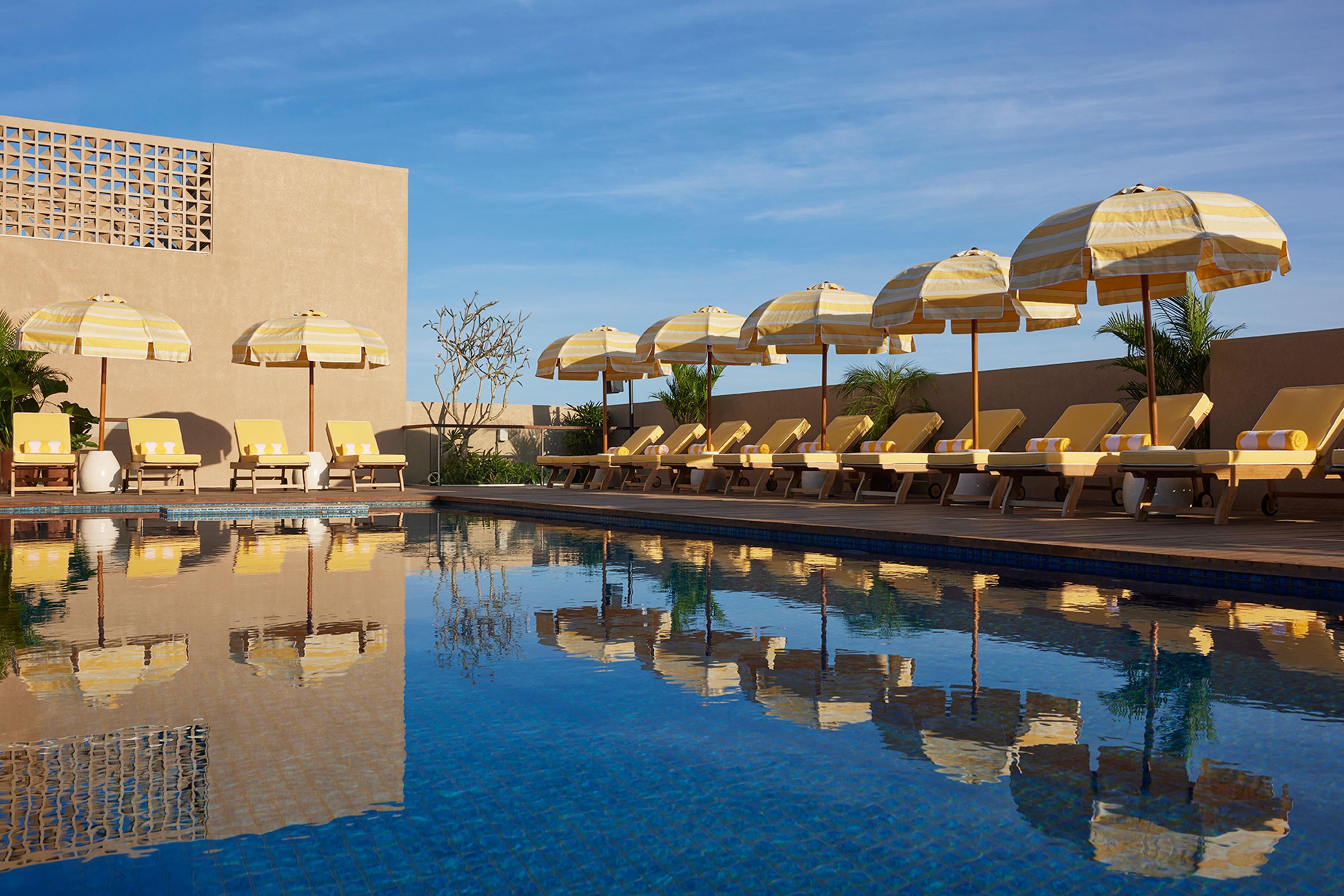 Una piscina al aire libre, sombrillas, sillones reclinables de piscina