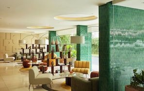 A modern lobby with a central seating area, a bookshelf, and a large window with a view of greenery. - Kleo Seminyak, part of JdV by Hyatt (Keroboken Kelod)