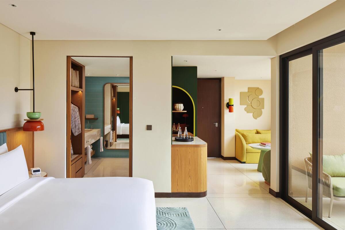A hotel room with a bed, a desk, a sofa, and a view through a glass door.