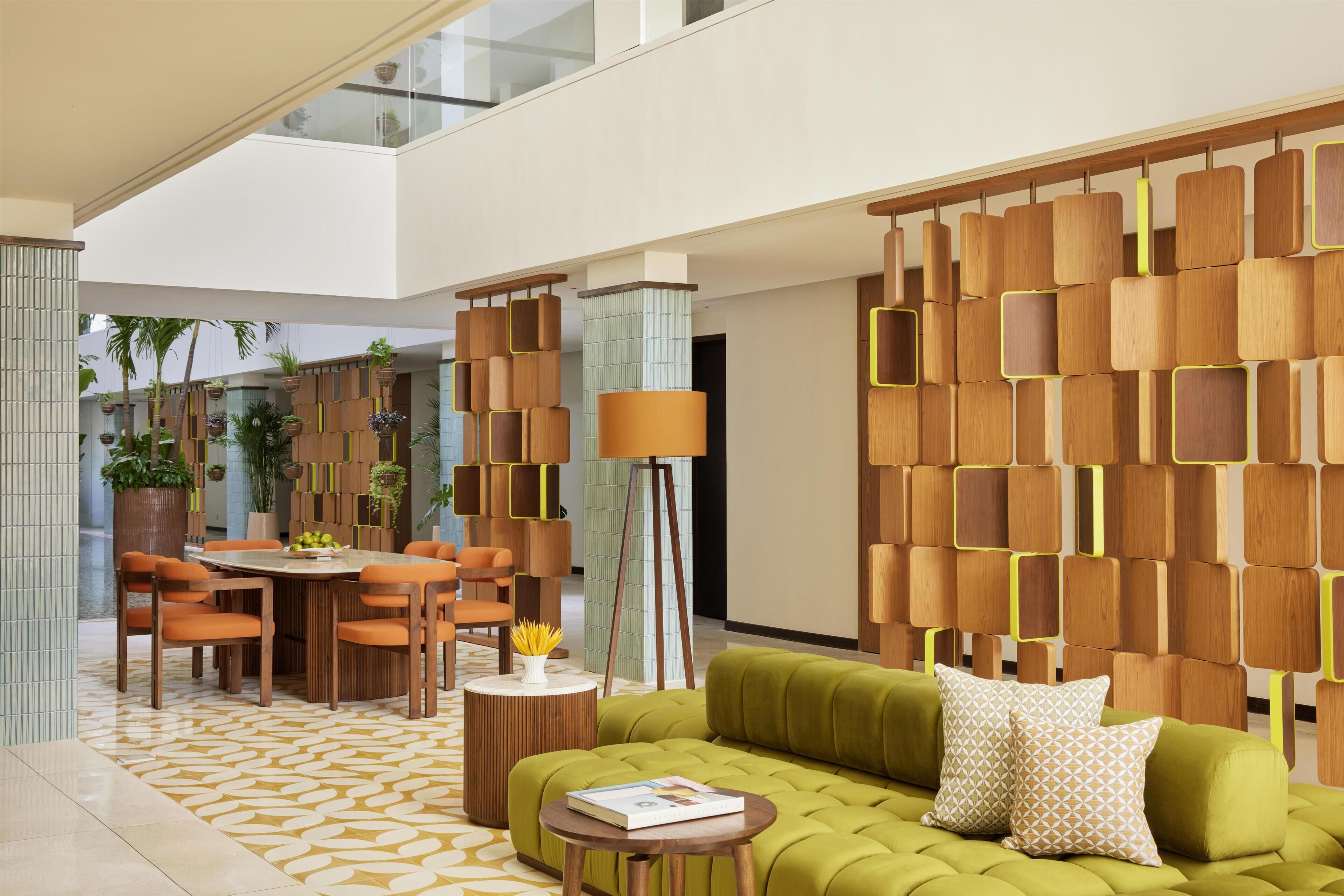 A modern interior with a green sofa, orange chairs, a dining table, and a decorative wall with geometric patterns.