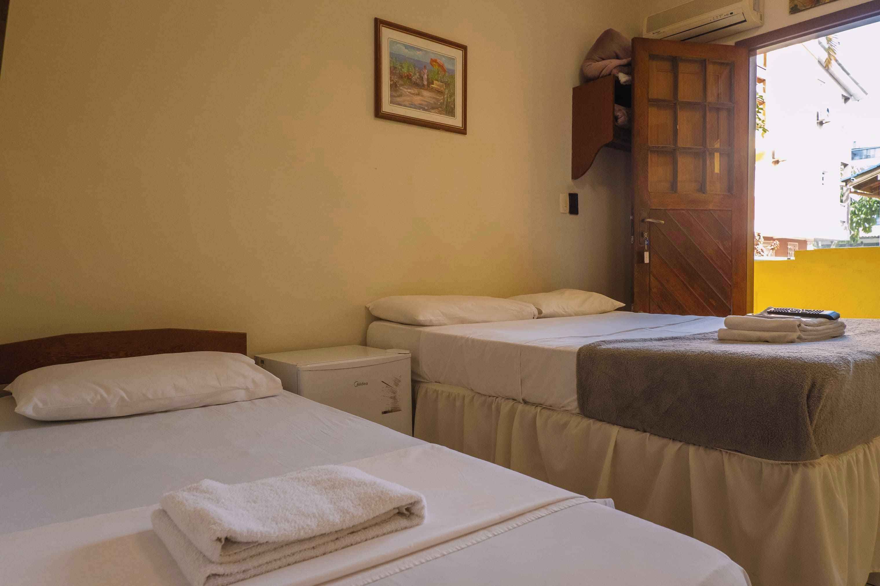 Habitación de hotel con dos camas, una mesita de noche pequeña, un aire acondicionado instalado en la pared y una puerta que da al exterior.