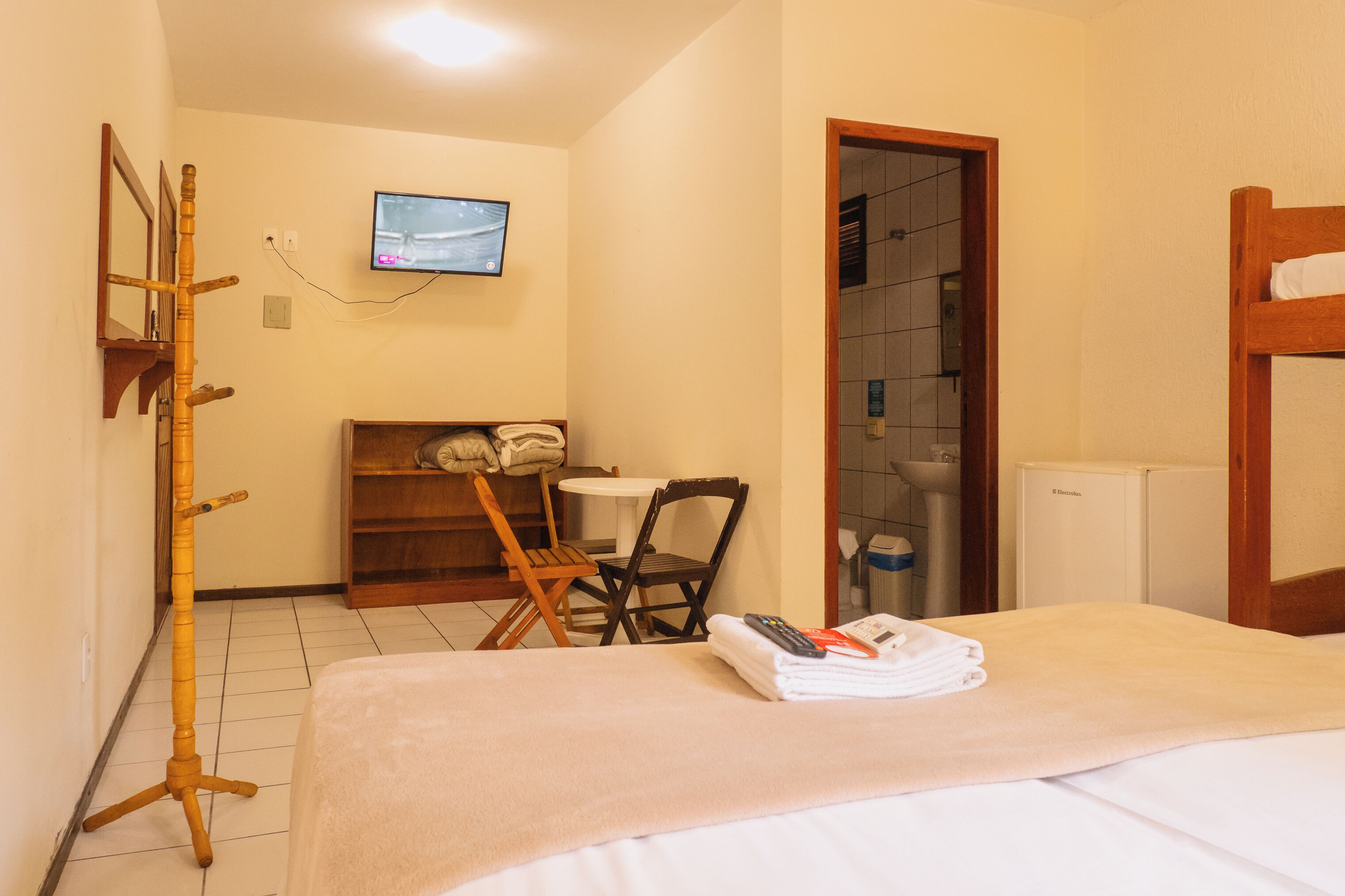 A hotel room with a bed, a wooden chair, a small table, a television, and a bathroom door.