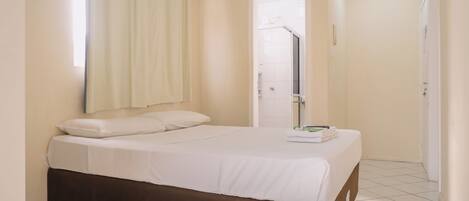 Uma cama de solteiro com cabeceira marrom em quarto com paredes brancas e piso de azulejos.