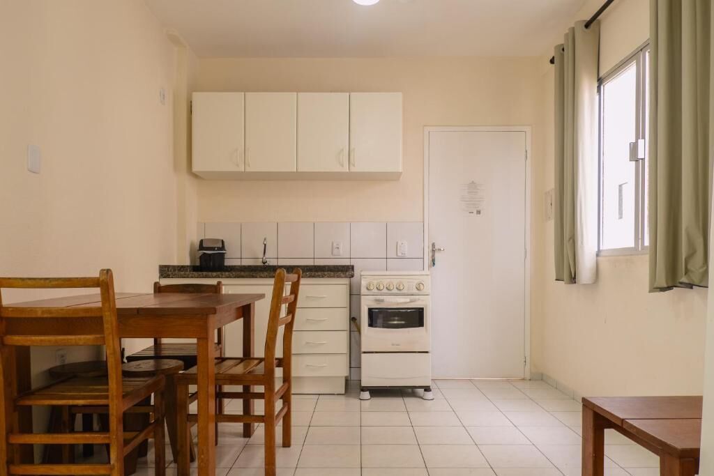 Cocina compacta con armarios blancos, horno pequeño y mesa de comedor con sillas.