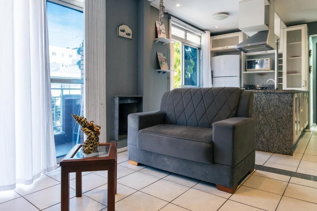 A modern living room with a grey sofa, a small wooden table with a giraffe figurine, and a kitchen area with cabinets and a microwave.