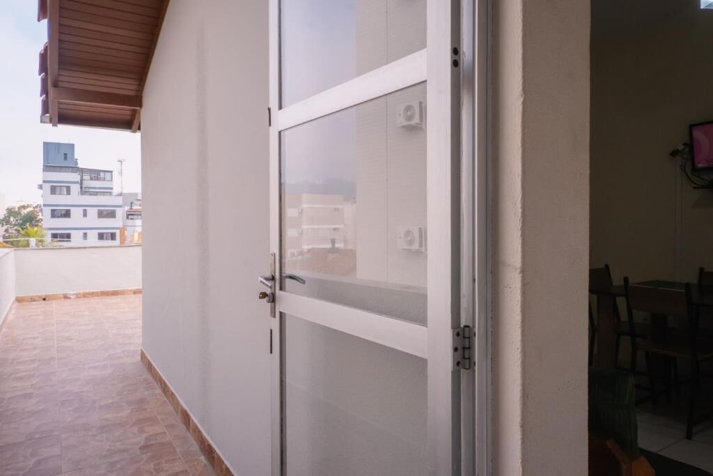 Une porte vitrée fermée donne accès à un balcon dont le sol est carrelé, avec un mur blanc et une vue dégagée sur l’extérieur.