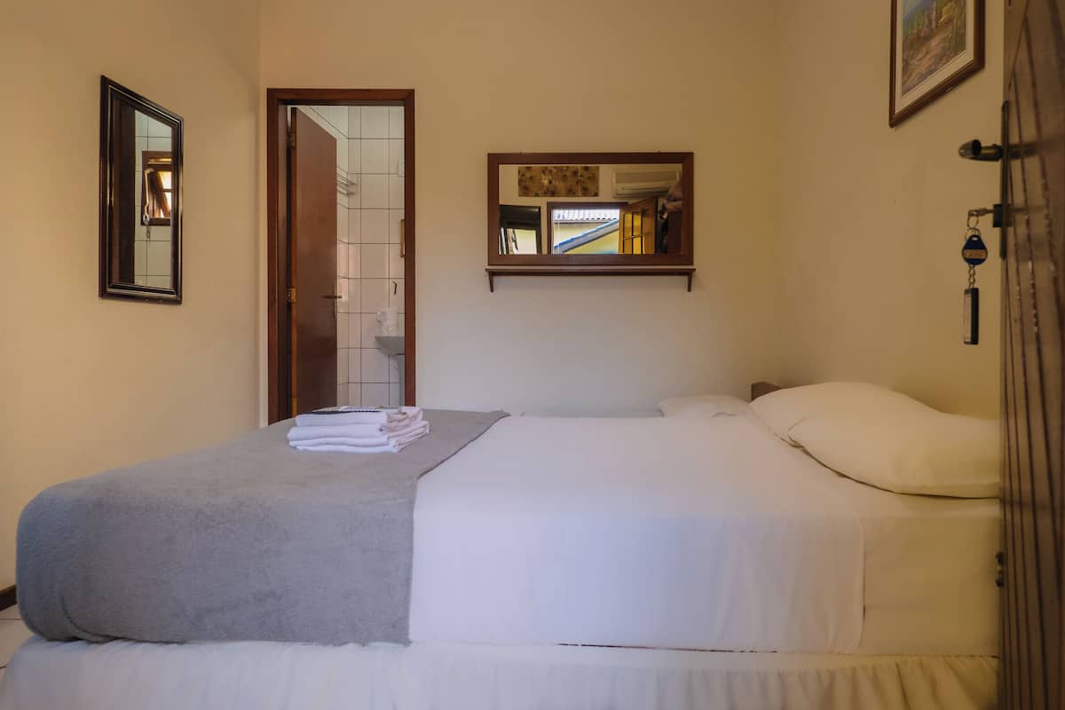A hotel room with a bed, a mirror, and a small window.