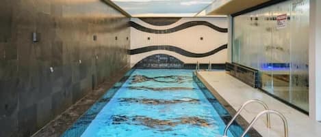 Una piscina interior con diseño de pared ondulada, superficie de agua cristalina y una escalera de piscina.