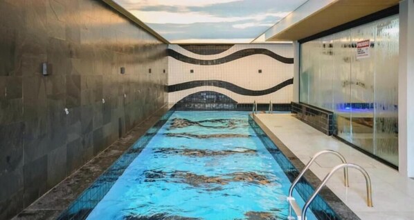 An indoor swimming pool with a wavy wall design, a clear water surface, and a pool ladder. - HANNA Amsterdam Hotel (Florianópolis)