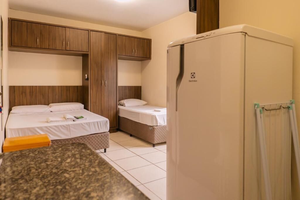 Ett hotellrum med två sängar, ett litet kök och ett kylskåp.