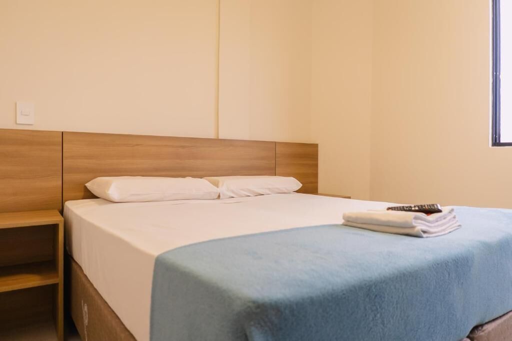 A hotel room with a wooden headboard, a bed with white bedding, a blue blanket, and a remote control on the bed.