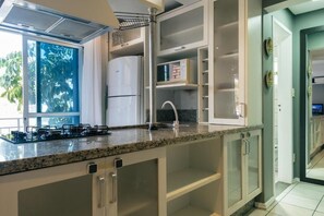 A kitchen with a built-in gas stove, a stainless steel refrigerator, and a window with a view of greenery. - HANNA Amsterdam Hotel (Florianópolis)