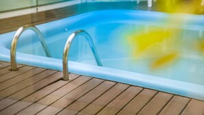 An indoor swimming pool with clear water, metal pool ladders, and a wooden deck. - HANNA Amsterdam Hotel & Events (Florianópolis)