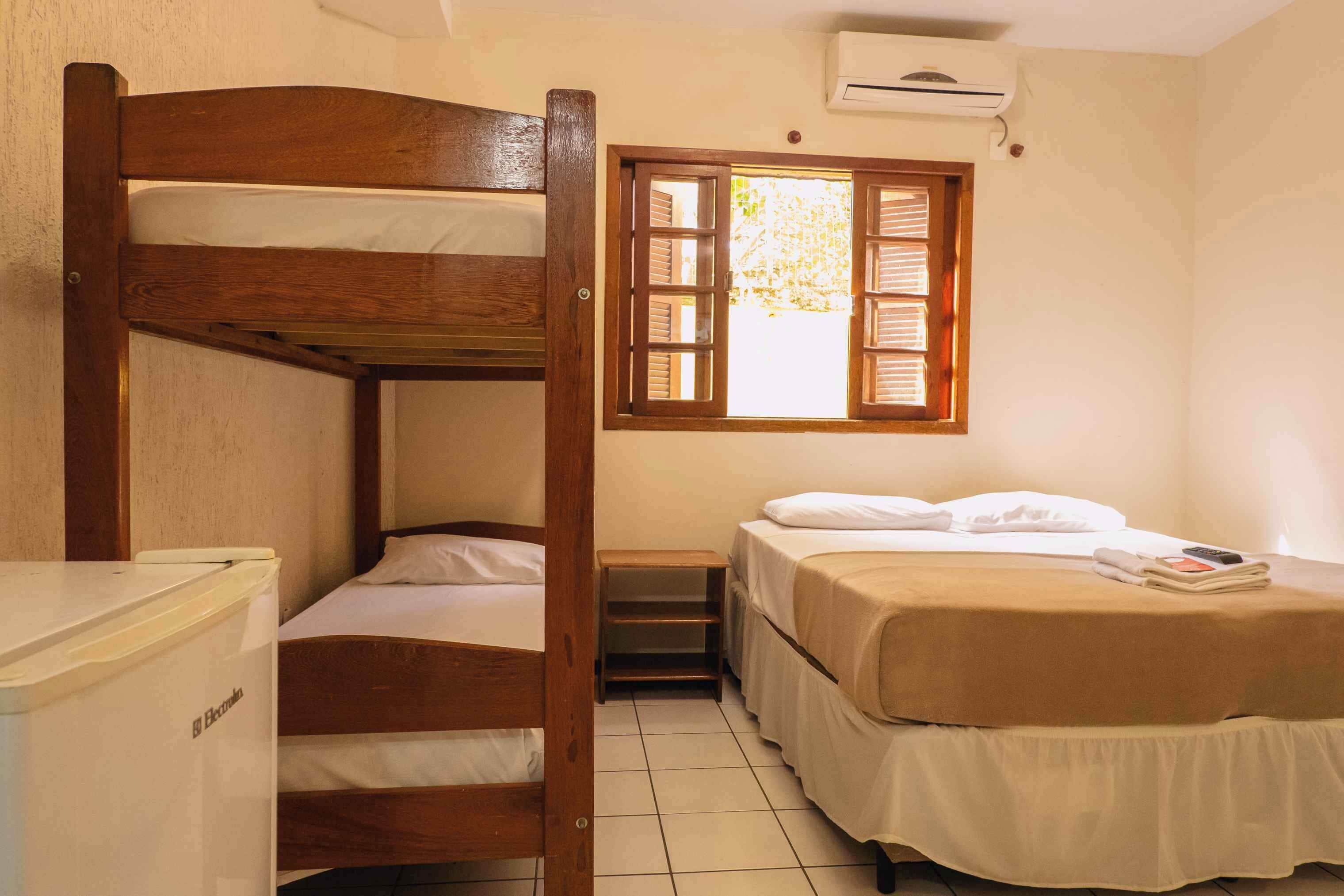 Une chambre avec un lit superposé, une petite table, une fenêtre avec des volets et un climatiseur fixé au mur.