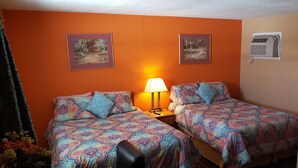 Ein Zimmer mit zwei Betten, jeweils mit gemusterten Bettbezügen, einem Nachttisch mit Lampe und zwei gerahmten Bildern an der Wand.