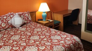 Ein Hotelzimmer mit einem großen Bett, einem Schreibtisch, einem Stuhl, einer Lampe und einem Spiegel.