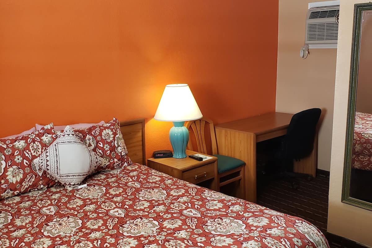 A hotel room with a large bed, a desk, a chair, a lamp, and a mirror.