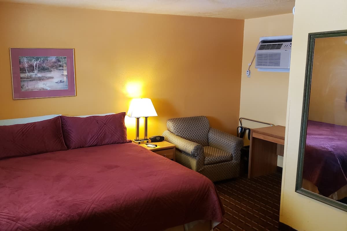 A hotel room with a large bed, a chair, a desk, and a mirror.