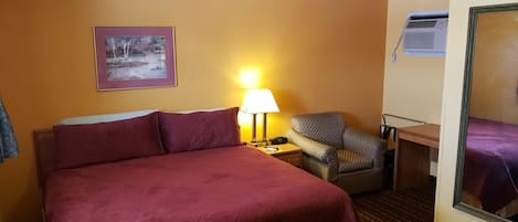 A hotel room with a large bed, a chair, a desk, and a mirror.