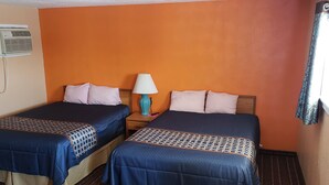 Ein Hotelzimmer mit zwei Betten, einer Klimaanlage, einem Nachttisch mit Lampe und einem Fenster mit Vorhängen.