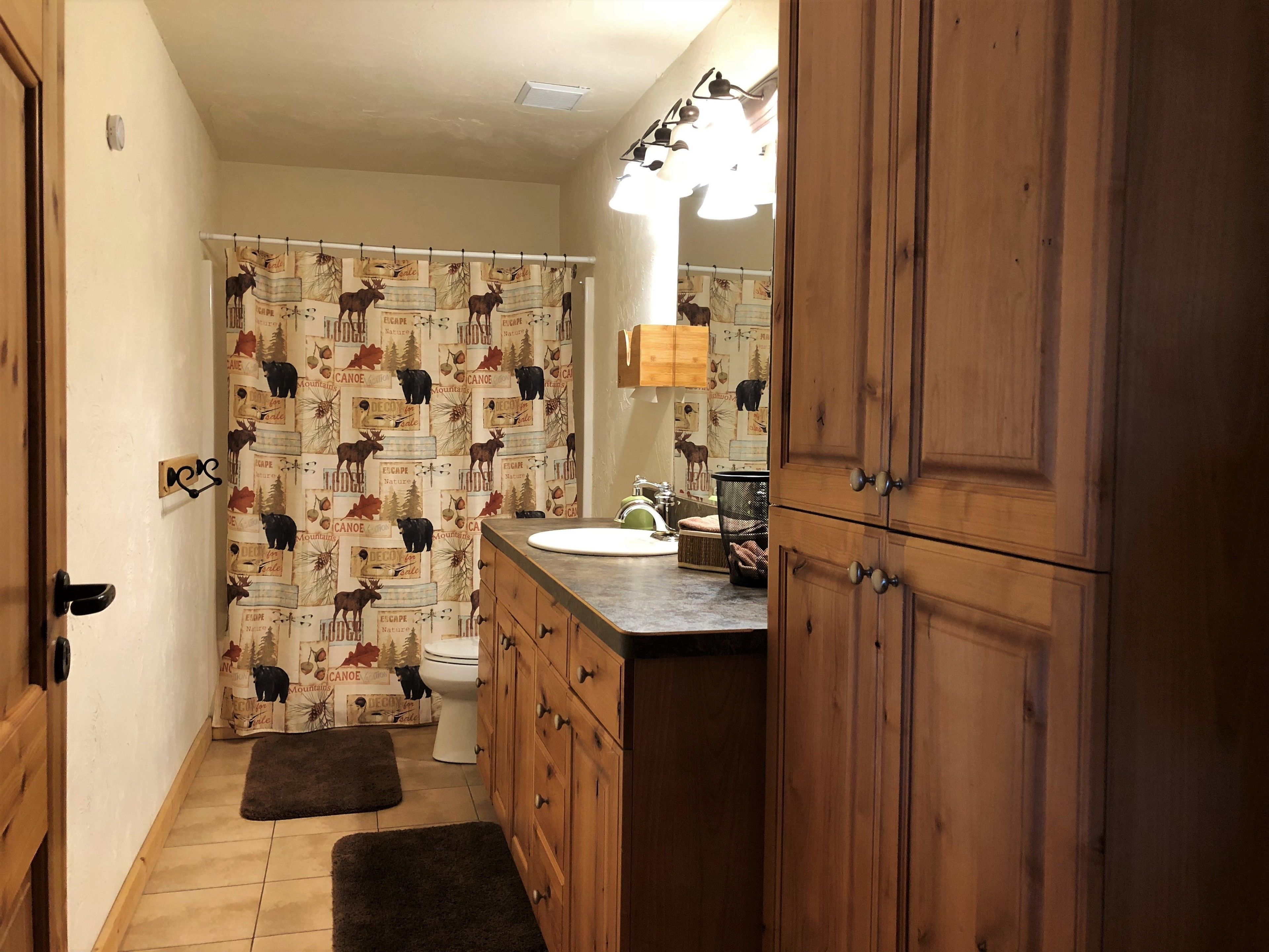 Une salle de bain avec des meubles en bois, des toilettes, un lavabo et un rideau de douche à motifs animaliers.